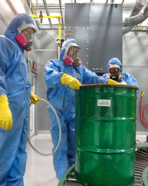 Men in hazard suits hadnling a waste drum